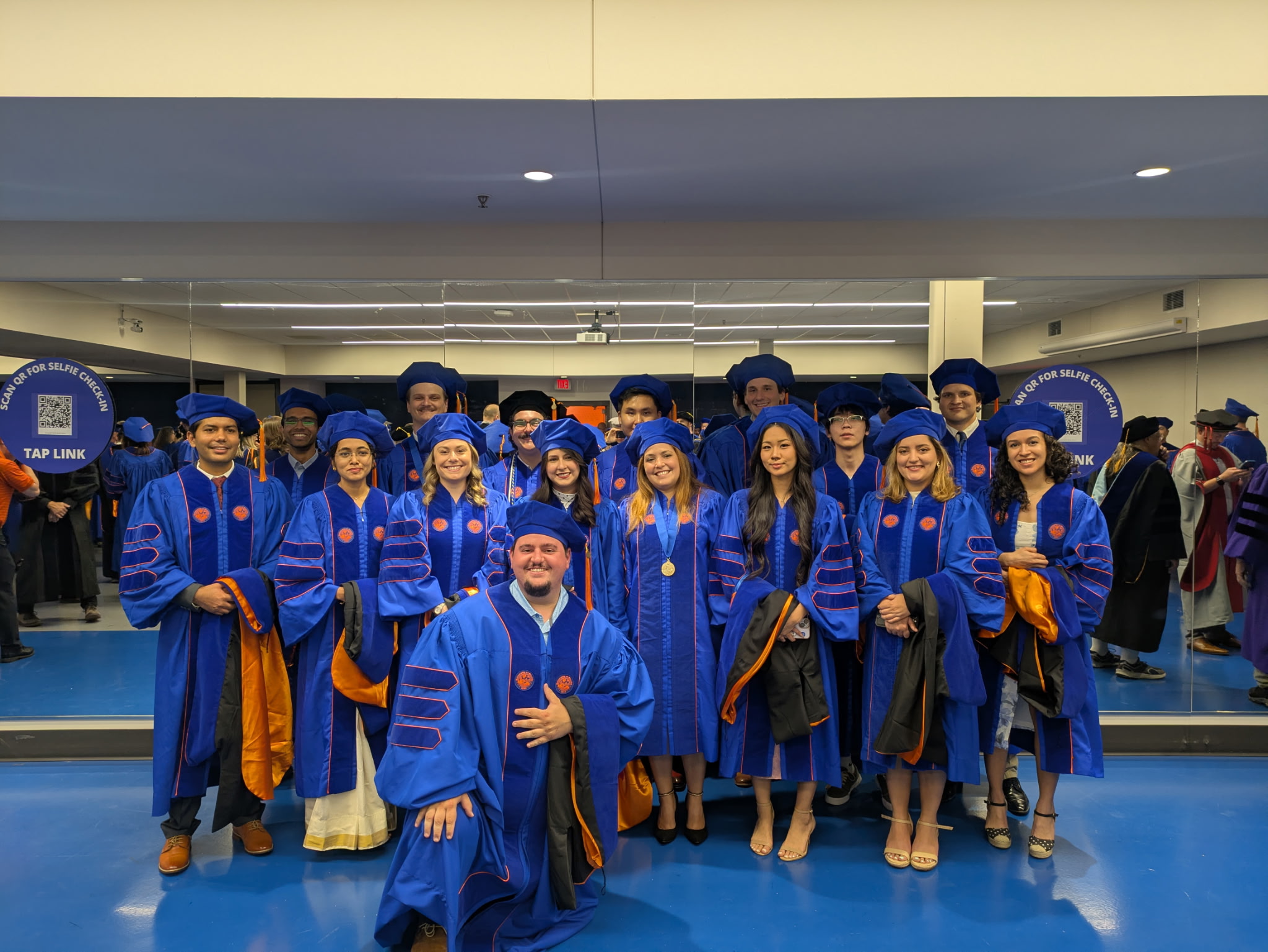 Group of people wearing blue graduation gowns and caps posing for a photo indoors